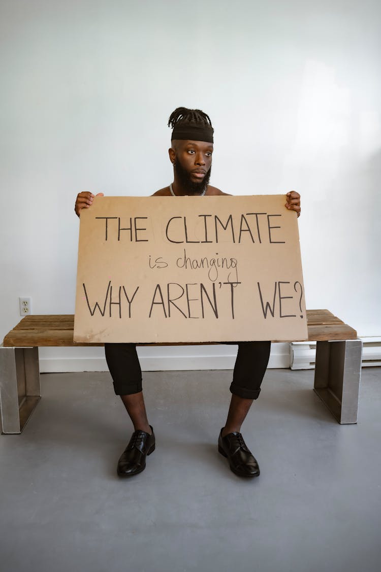 A Sad Man Sitting On A Wooden Bench While Holding A Placard