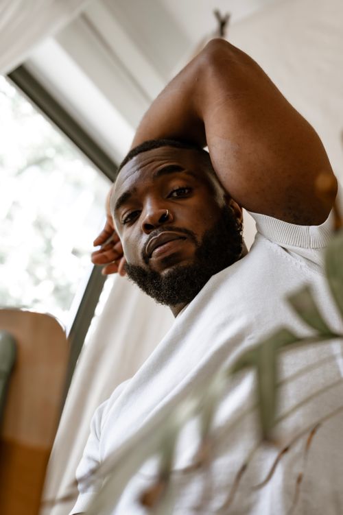 Free Low angle shot of a bearded African American man with a nose piercing, posing indoors in a white shirt. Stock Photo