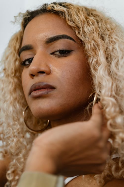 Free Close-up portrait of a confident woman with blonde curly hair and hoop earrings looking at the camera. Stock Photo