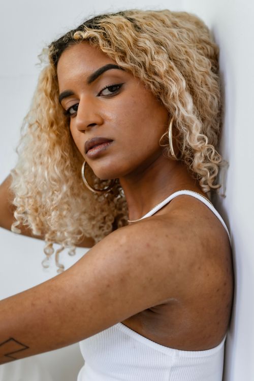 Free Close-up of a stylish woman with curly blonde hair and hoop earrings looking confidently at the camera. Stock Photo