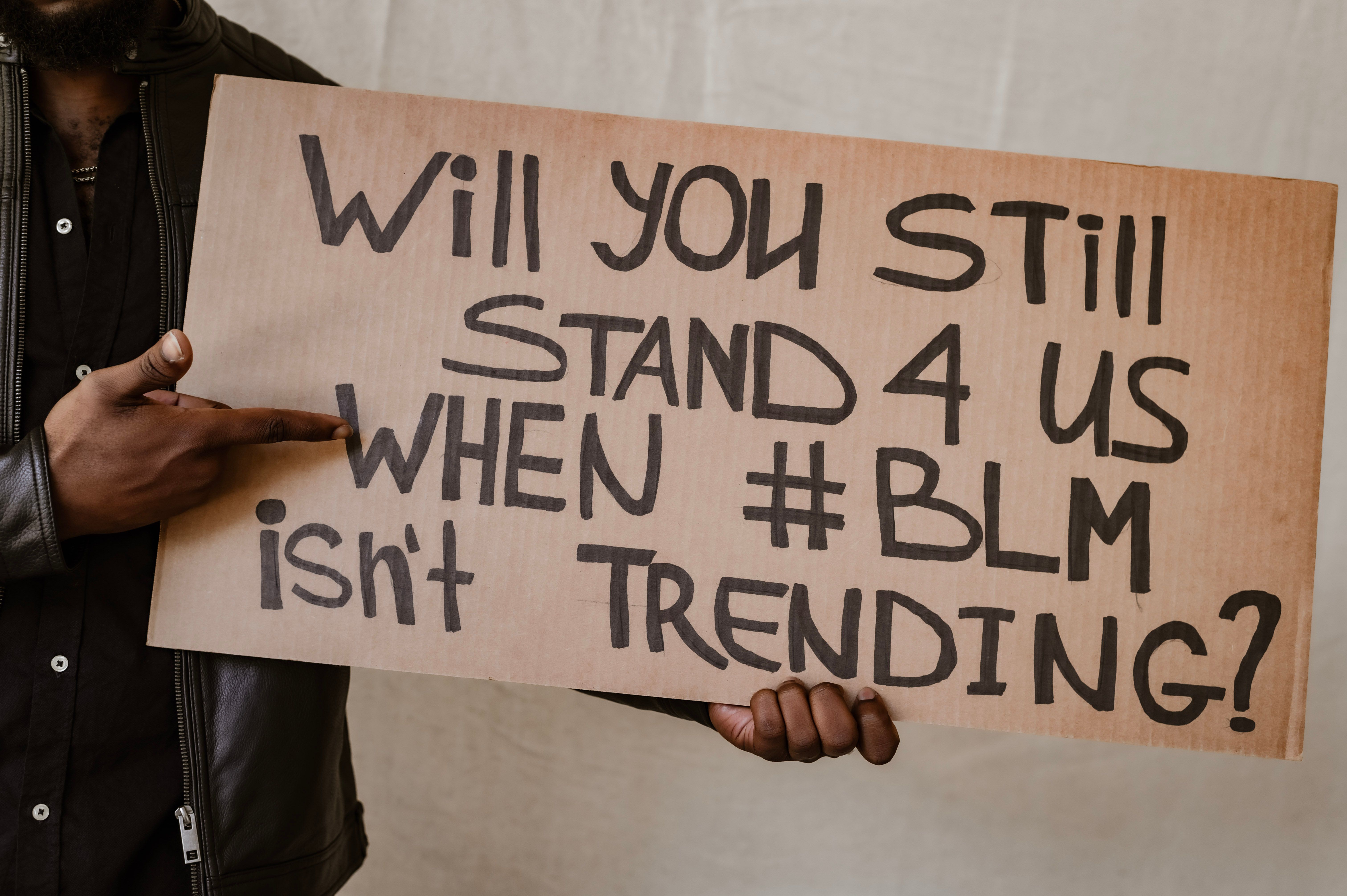 Close-up of Gen Z hands holding a protest sign with a spiritual/justice-oriented quote next to a phone displaying a social justice infographic