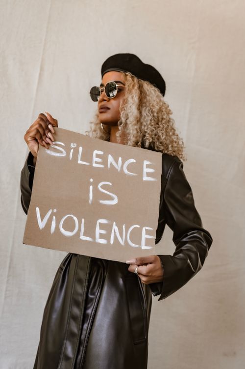 Free Stylish African American woman holding a protest sign with message 'Silence is Violence' indoors. Stock Photo