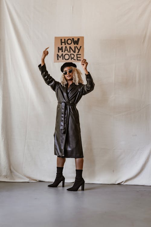 A Woman in a Leather Trench Coat Holding and Pointing at a Placard