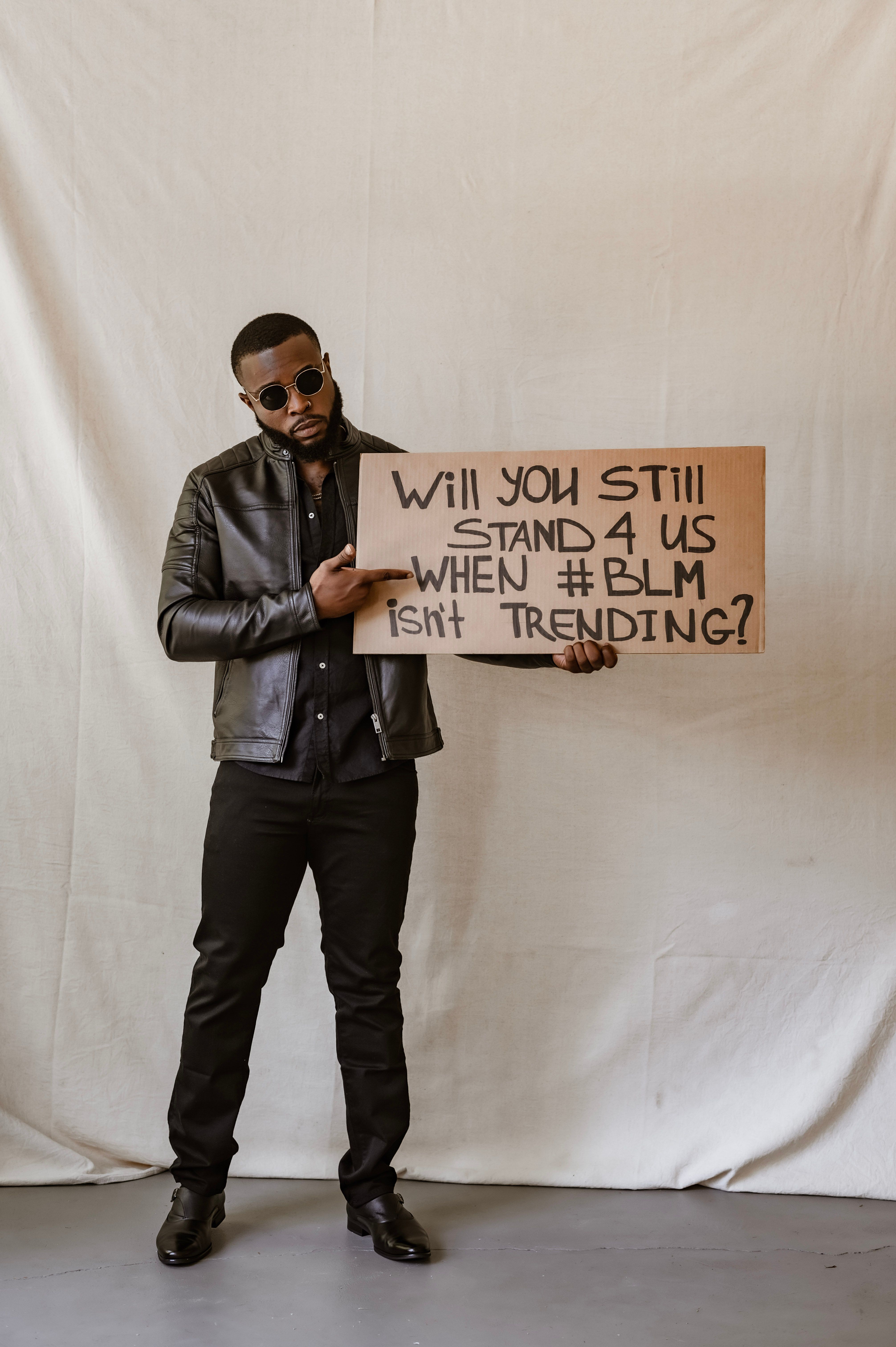 Man holding a sign supporting BLM movement in an indoor setting, wearing a leather jacket.