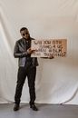 Man in Black Leather Jacket Holding Brown Cardboard with Text