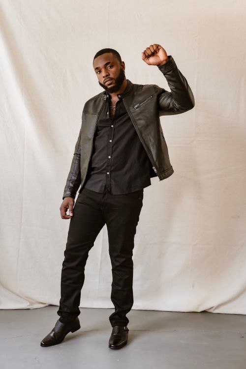 Free A fashionable black man in a leather jacket poses with a raised fist in a studio setting. Stock Photo