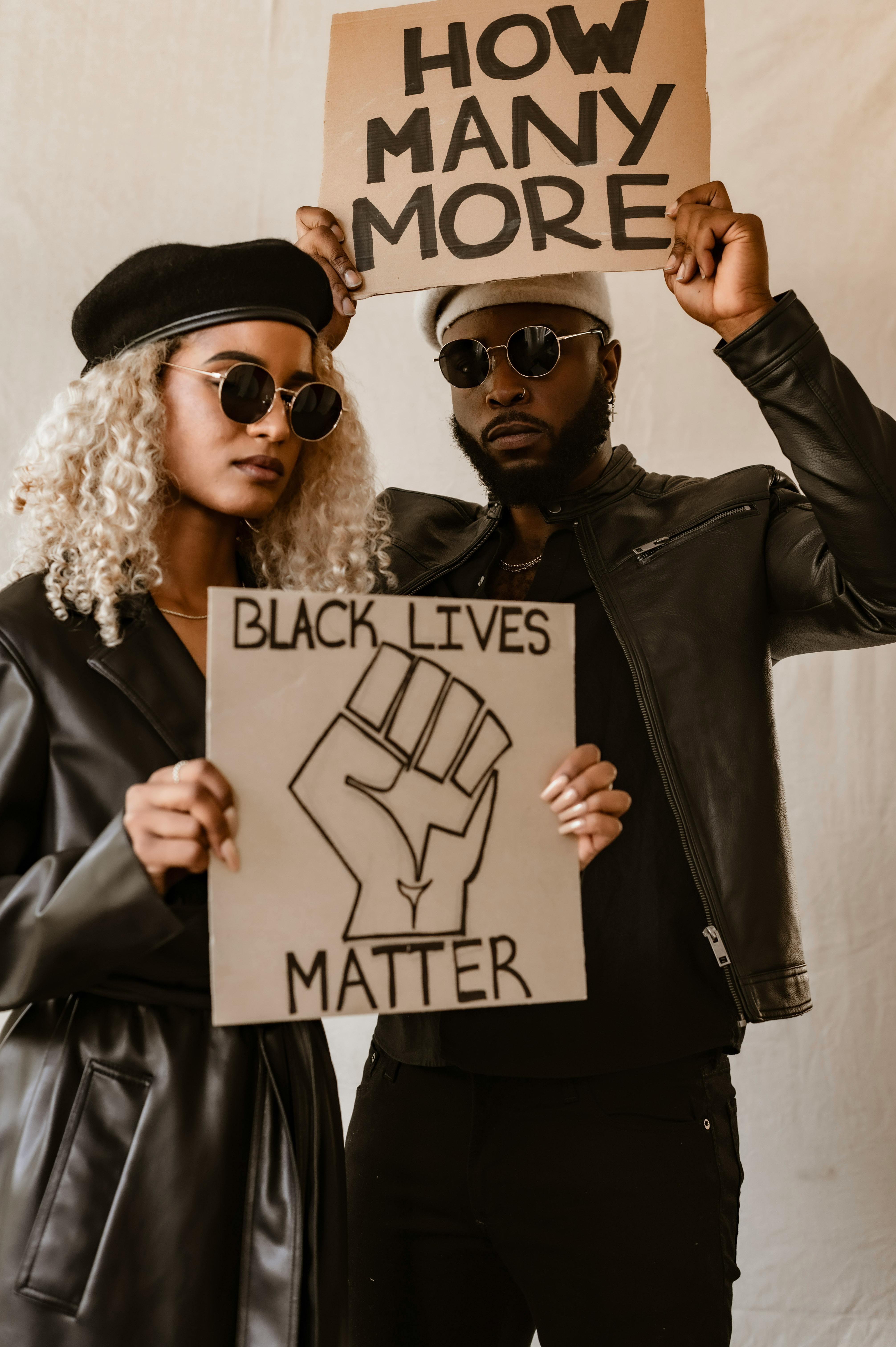 a man and a woman wearing black leather outfit holding placards while posing at the camera