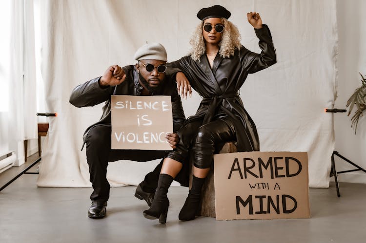 A Couple In Leather Wear Holding Posters