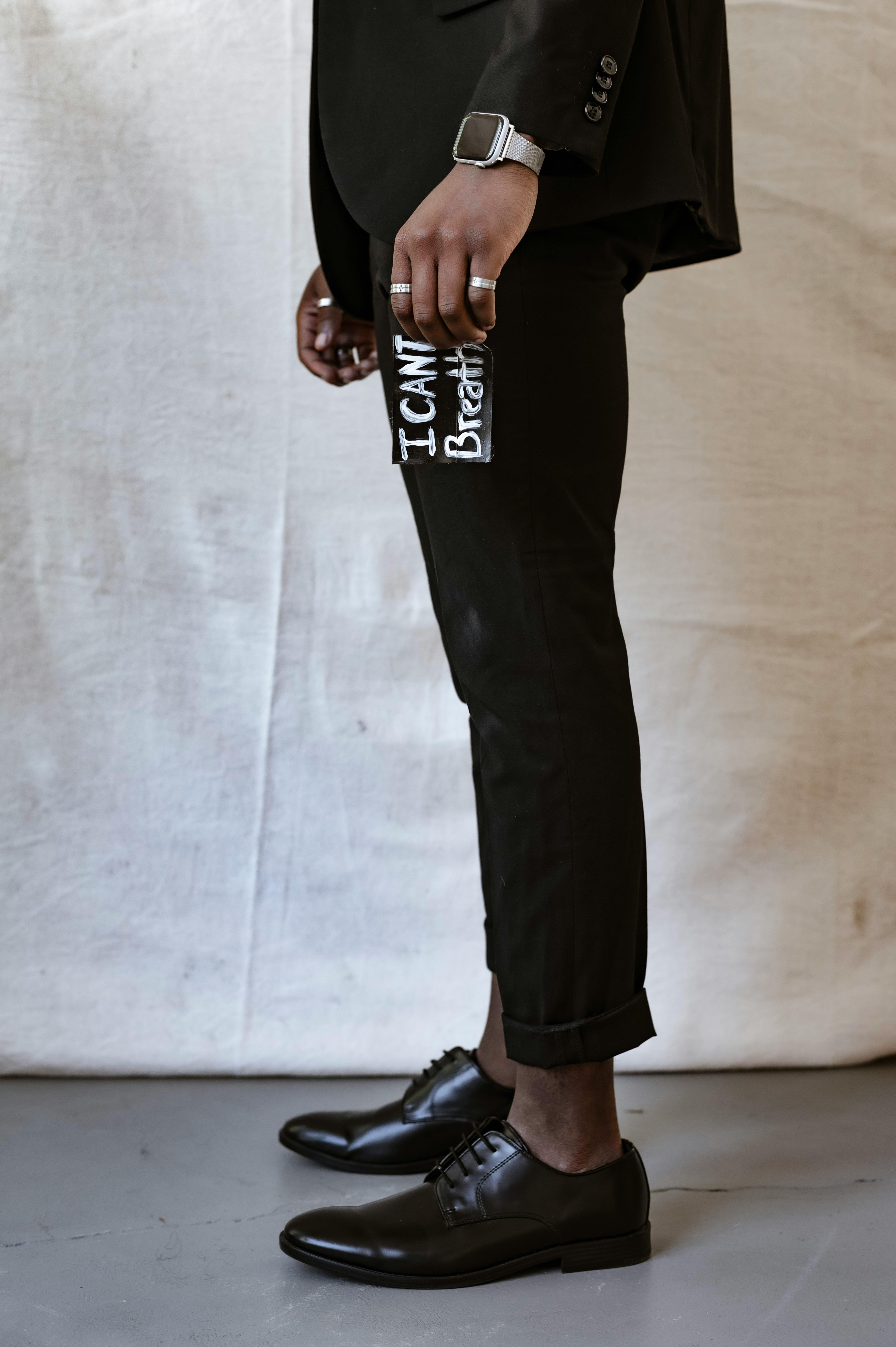Close-up of a man wearing black pants with social message print and formal shoes.