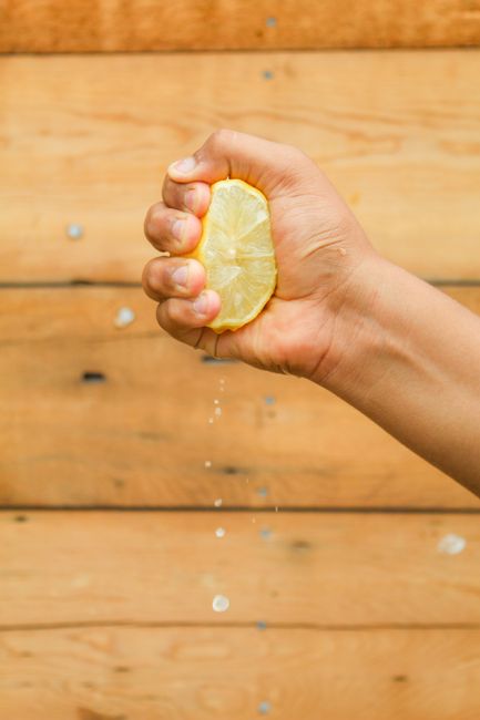 Close-up of a hand squeezing a lemon, with juice droplets captured mid-air against a wooden background.