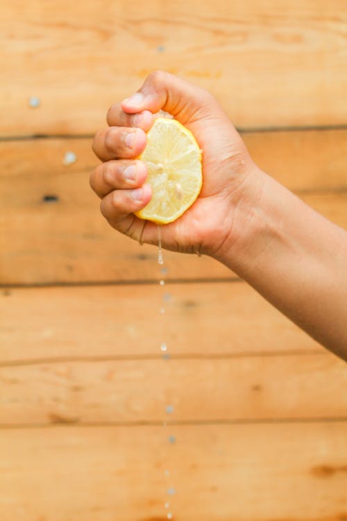 Close-Up Photo of a Person Squeezing a Juicy Lemon