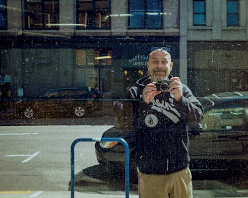 A Smiling Man in Black Hoodie Taking Photos Using a Camera