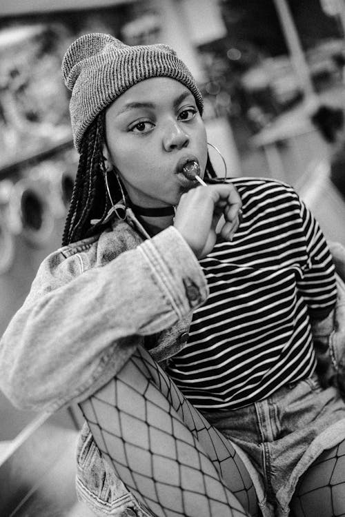 A Woman with Afro Hair Wearing Striped Shirt while Licking a Stick of Lollipop