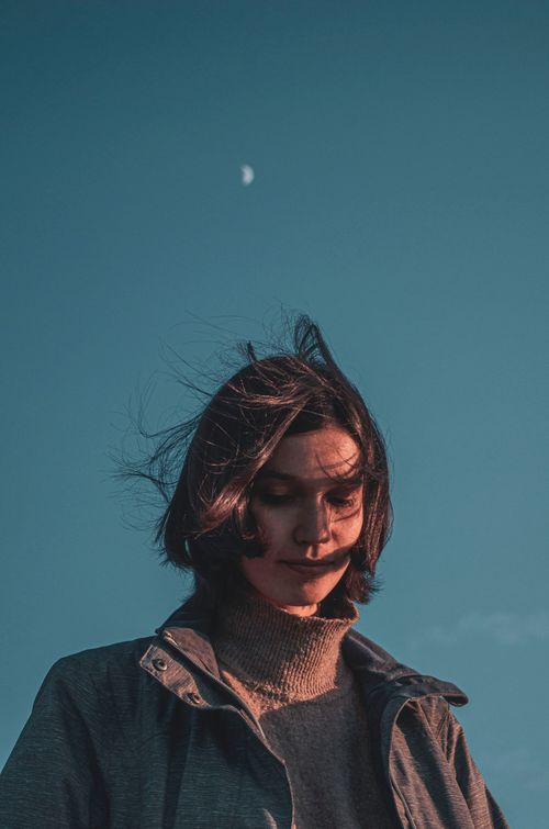 Free A woman with windswept hair gazes down under a blue sky with a visible moon. Stock Photo
