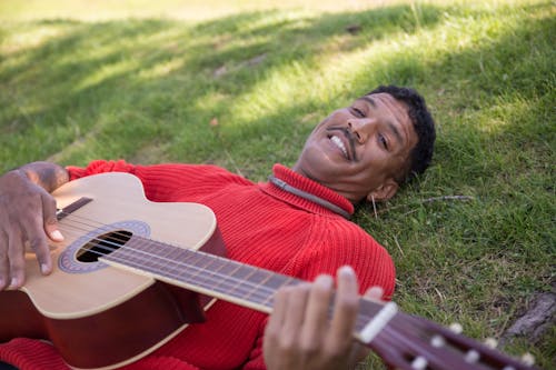 A Man Lying on a Grassy Ground while Playing a Guitar