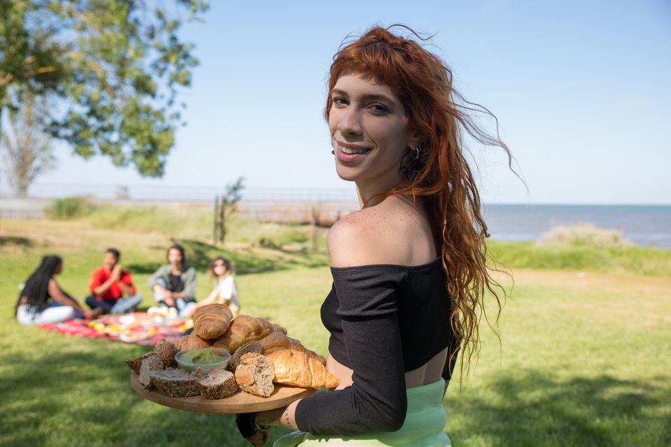Woman holding a tray of bread at a coastal picnic in Portugal, enjoying a sunny day with friends.