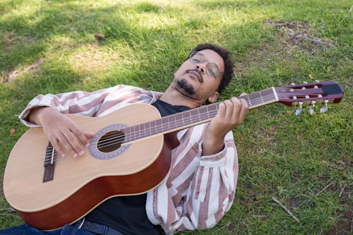 A Man Lying on the Gras Playing the Acoustic Guitar