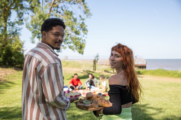 A Couple Serving Food For Their Friends At The Picnic Grounds