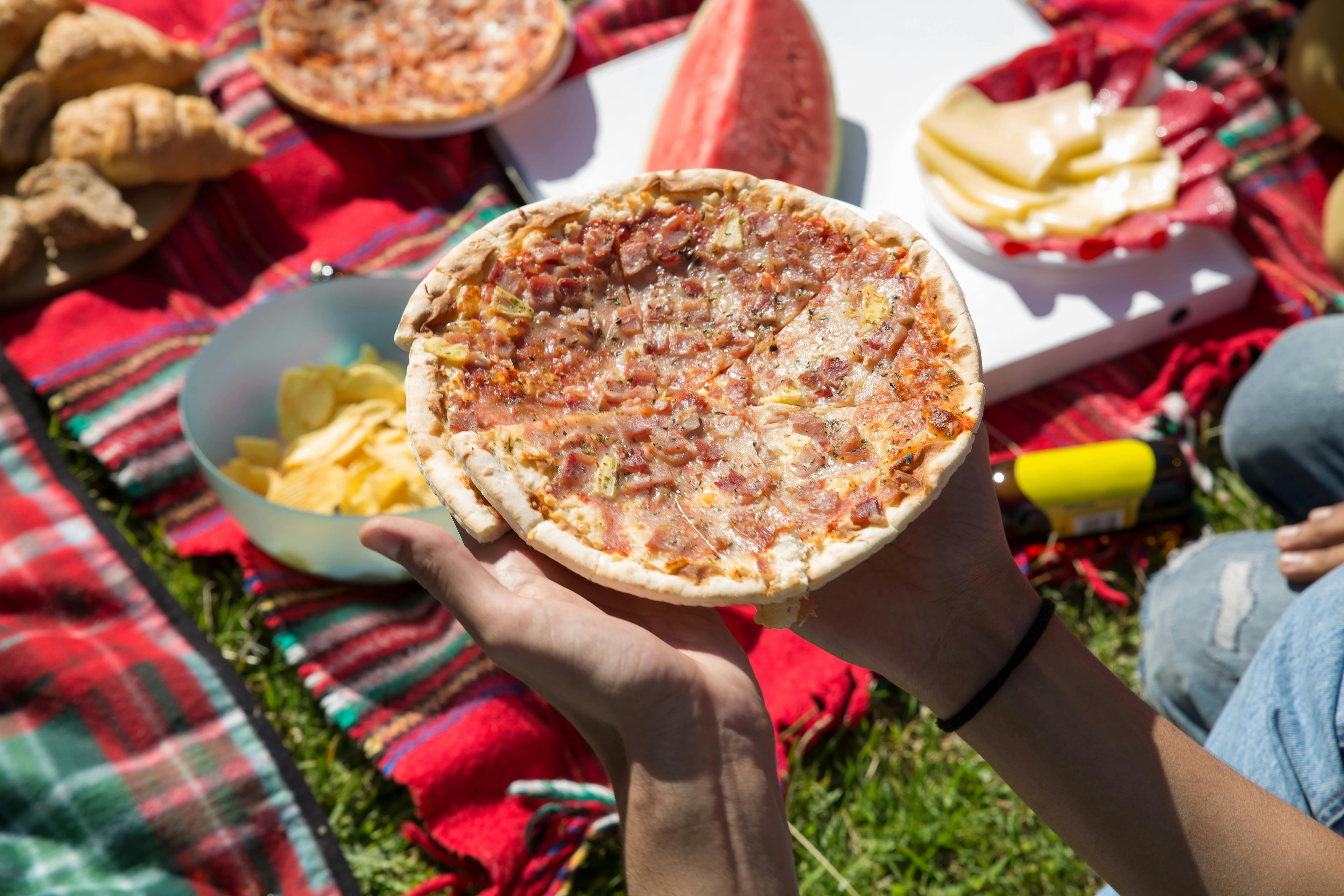 Hands holding pizza at an outdoor picnic on a sunny day in Portugal.