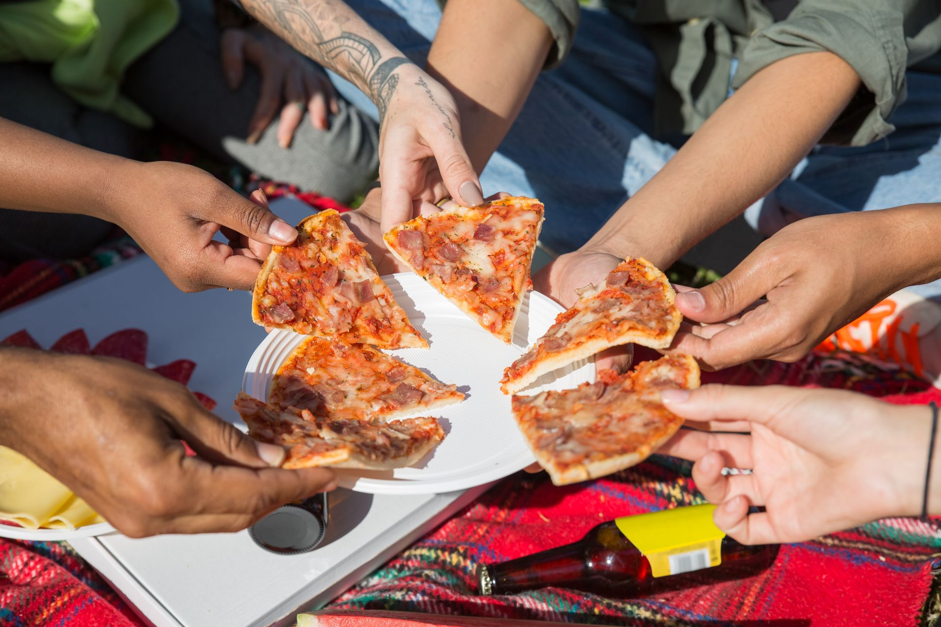 Group of diverse friends sharing pizza slices during a sunny outdoor picnic in Portugal.