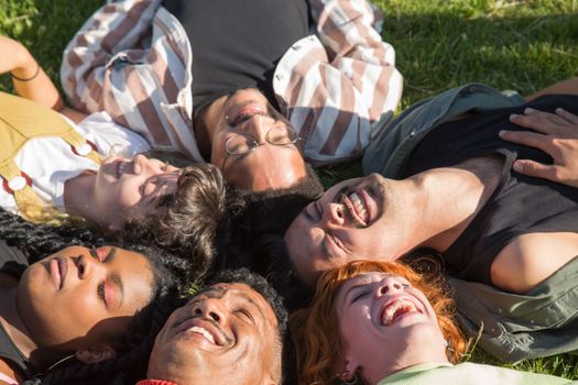 A diverse group of friends lying in the grass, laughing under the sunny sky, showcasing joy and togetherness.
