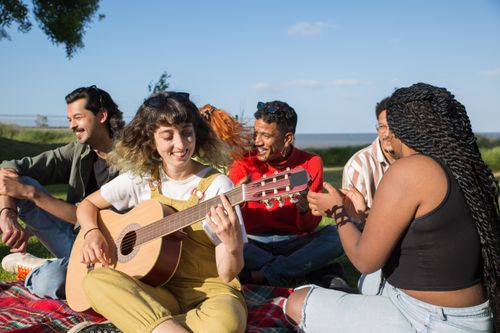 Free A diverse group of friends enjoying a sunny day outdoors, playing guitar and having fun in a park. Stock Photo