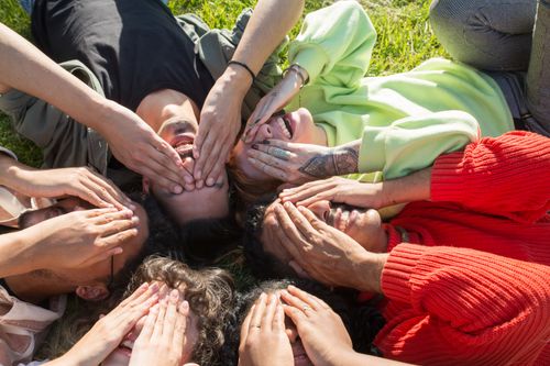 Free Diverse group of friends lying on grass, covering eyes, enjoying a sunny day outdoors. Stock Photo