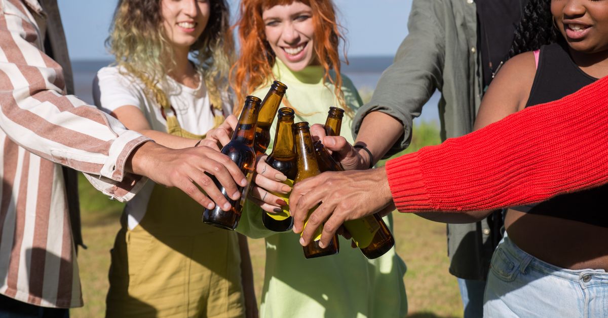 A diverse group of friends outdoors toasting with beer bottles, enjoying a sunny day.