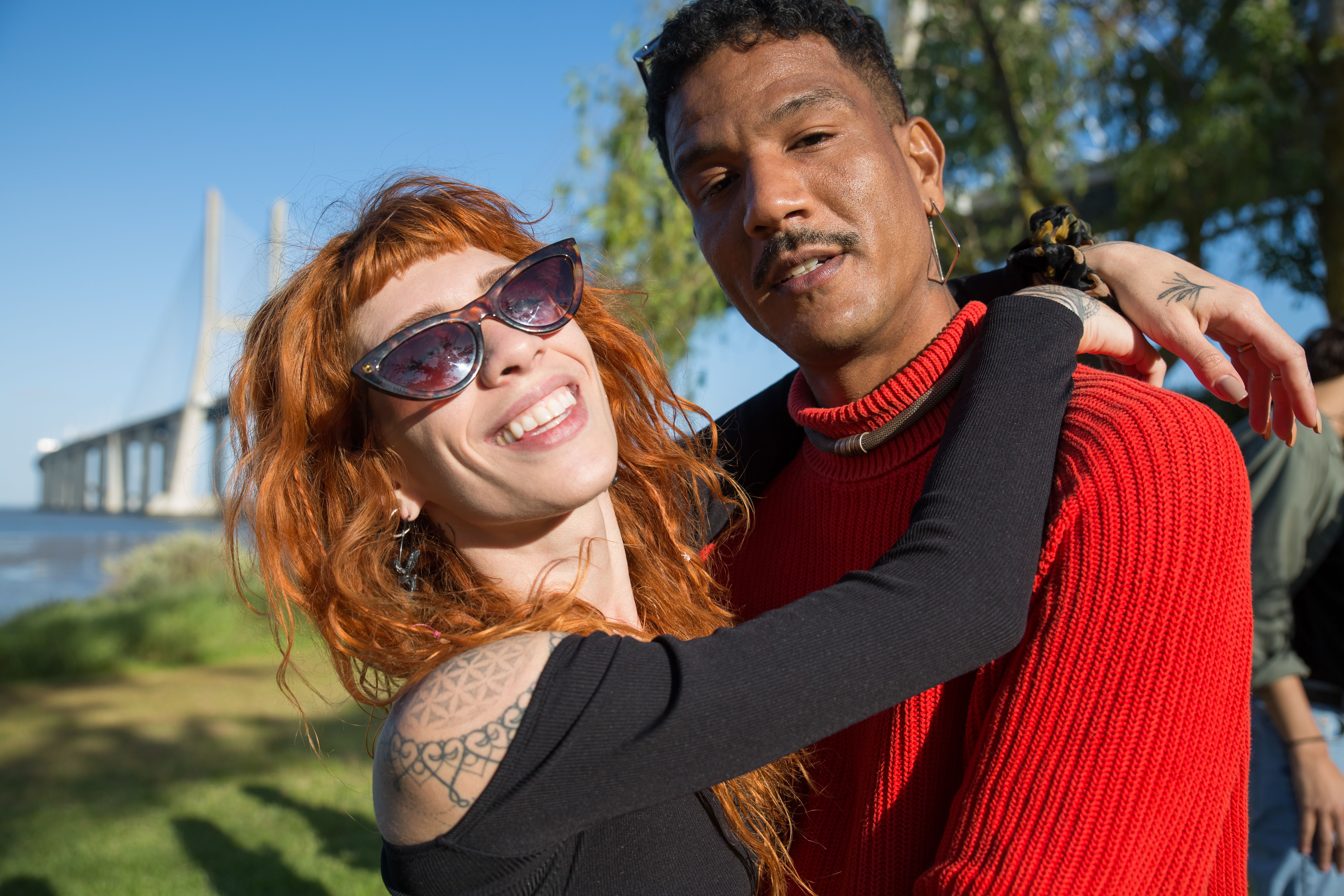 Cheerful couple embracing outdoors near Vasco da Gama Bridge in Lisbon.