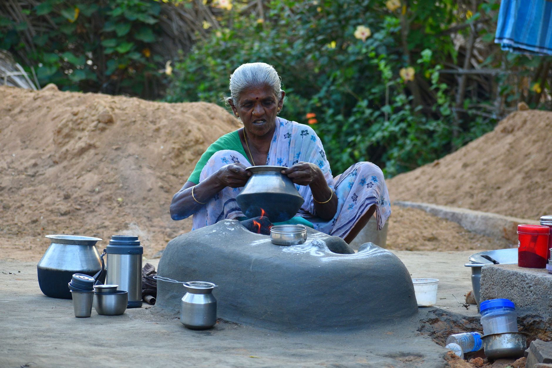 Elderly woman cooking outdoors in rural India using traditional methods.