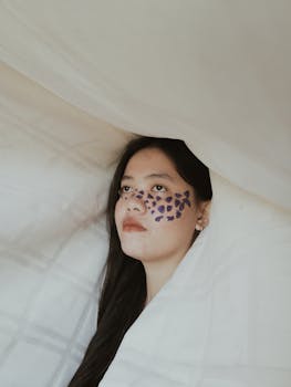 Creative portrait of a woman with artistic face paint surrounded by soft fabric, creating a dreamy ambiance.