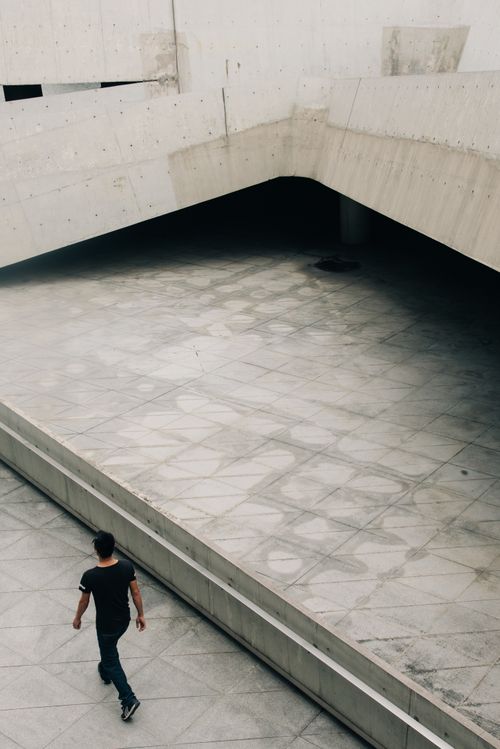Free A solitary figure walks in a modern urban space with minimalistic architecture. Stock Photo