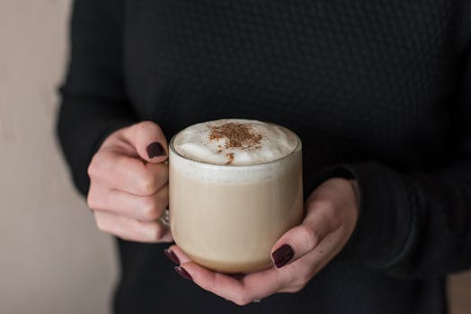 Close-up of a warm cappuccino held in hands with dark nail polish.
