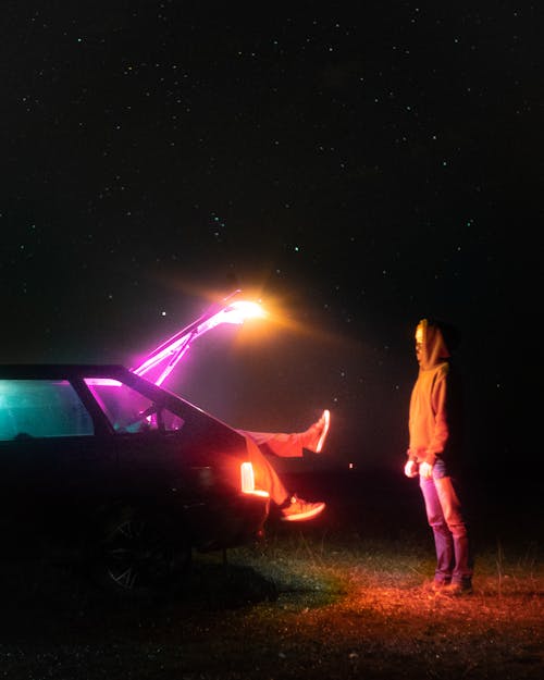 Man in White Long Sleeve Shirt Standing Beside Car during Night Time