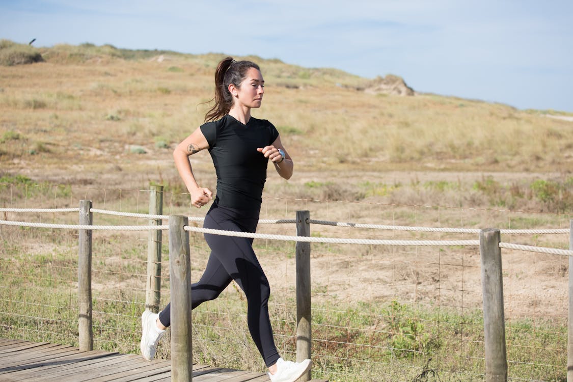 Free Woman in Black Activewear Running on a Boardwalk Stock Photo