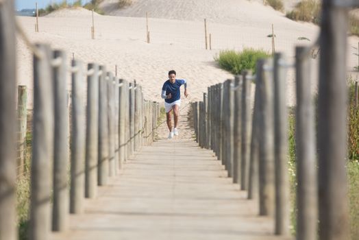 Man in activewear running on a wooden boardwalk at a scenic beach. Perfect for fitness and lifestyle themes.