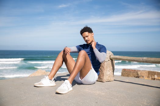 Young adult man sitting by the seaside on a sunny day, dressed in activewear.