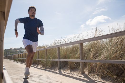 Athletic man running on a sunny coastal boardwalk in Portugal, showcasing fitness and determination.