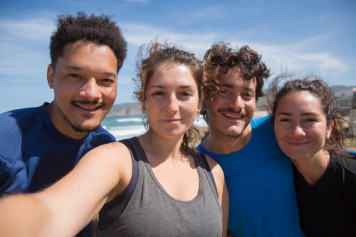 Free Four young adults smiling at the beach, capturing a joyful moment under the sunny sky. Stock Photo