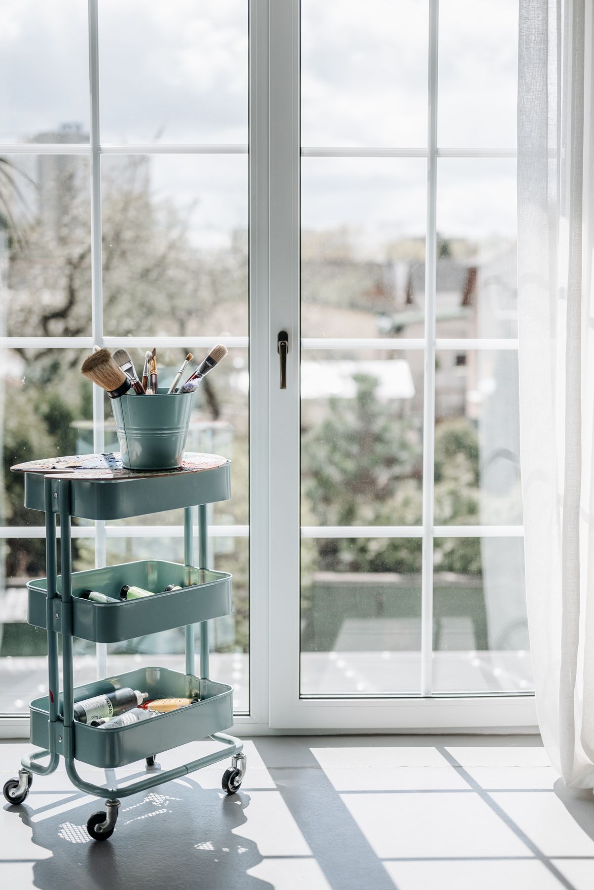 Three-tier rolling cart with craft supplies by a window