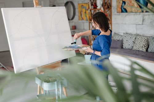 Free A woman in blue clothing paints on a large canvas in a bright and modern studio setting. Stock Photo