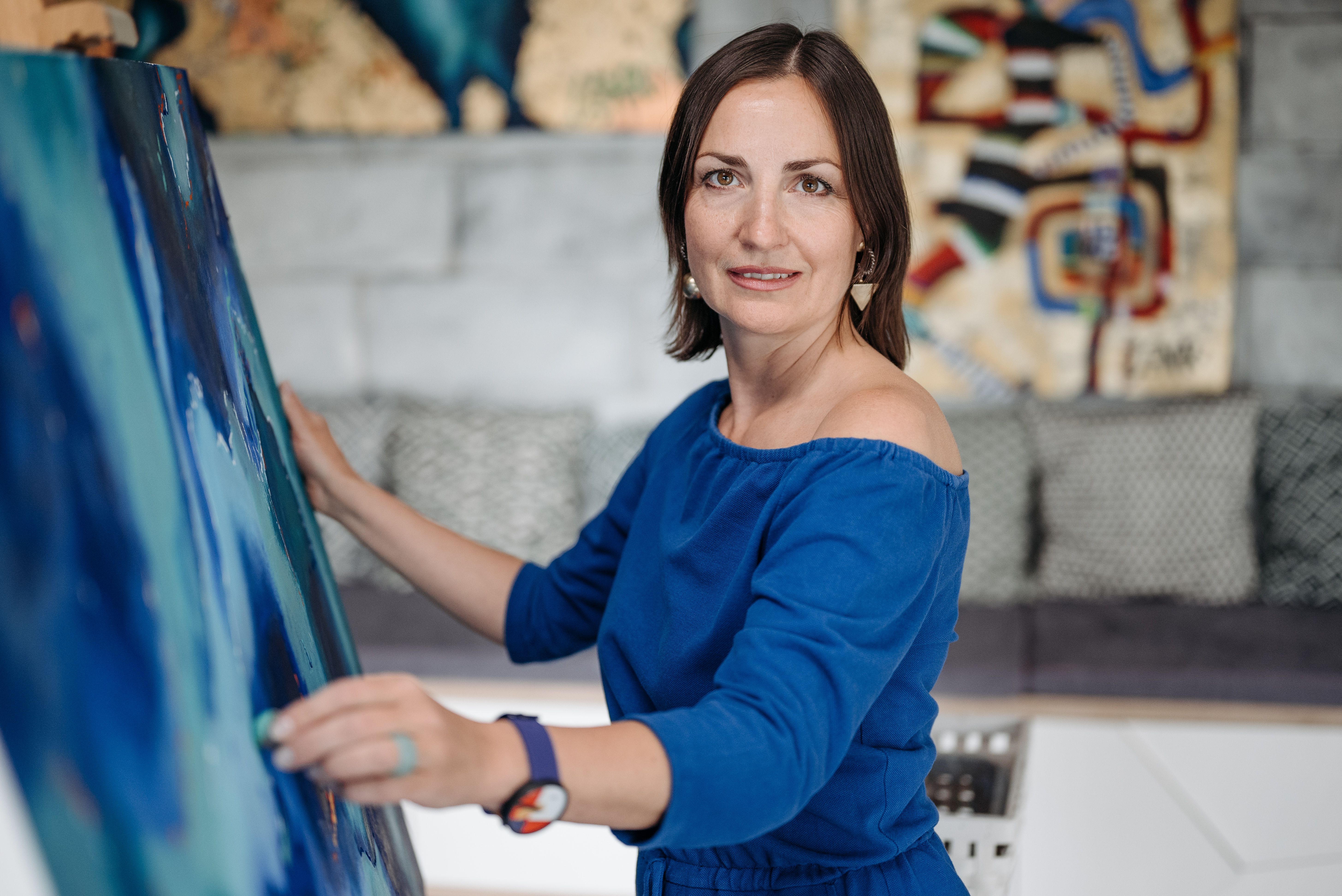 A woman artist in a blue outfit painting a large canvas in her studio.