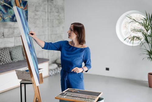 Free An adult woman paints on a canvas inside a modern, bright studio room. Stock Photo