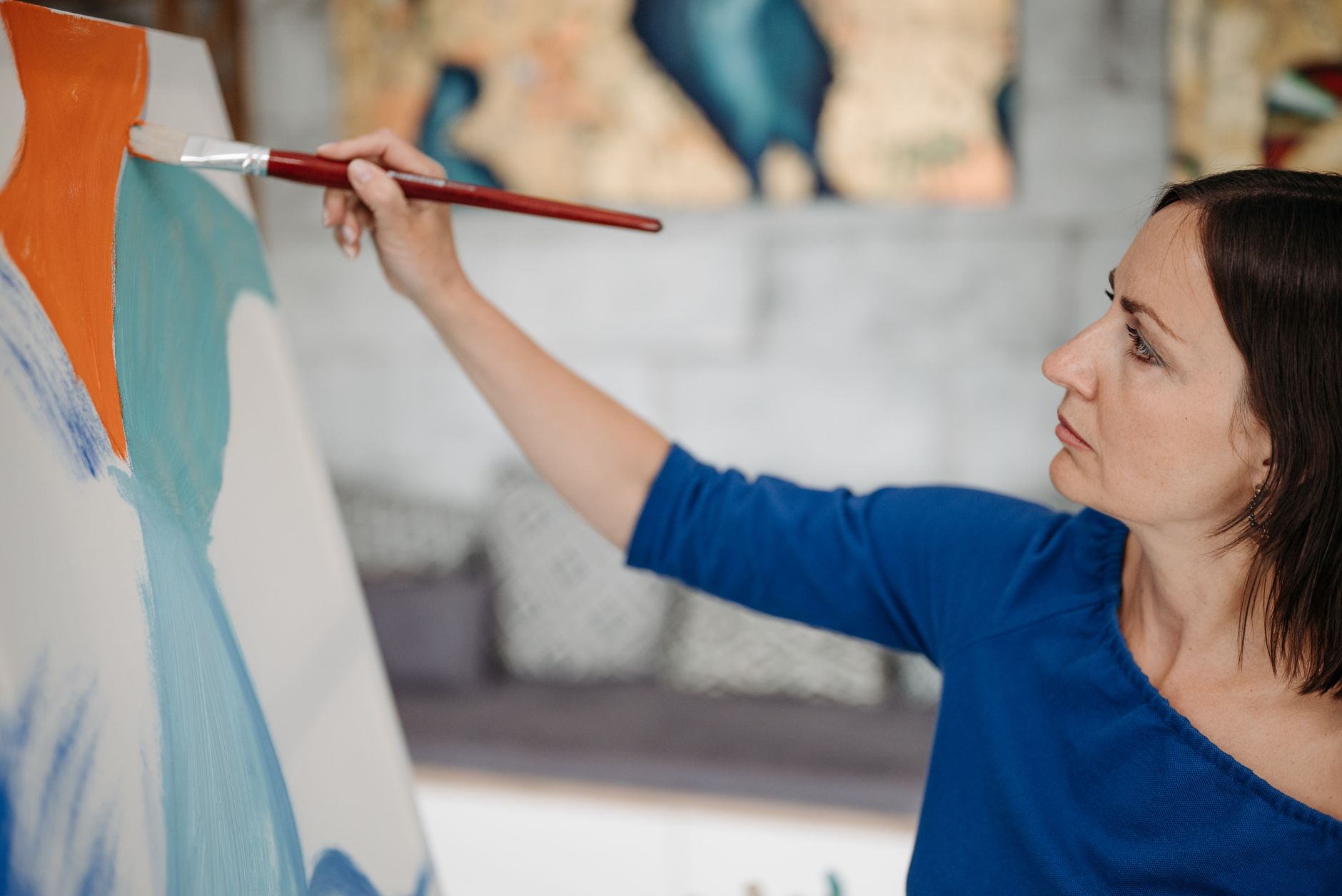 Focused woman painting a colorful artwork on canvas indoors.