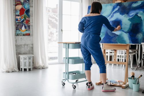 Free Woman in blue painting abstract art in a bright studio. Creative and serene atmosphere. Stock Photo