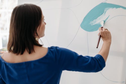 Woman in Blue Top Holding a Paint Brush Against a White Canvas