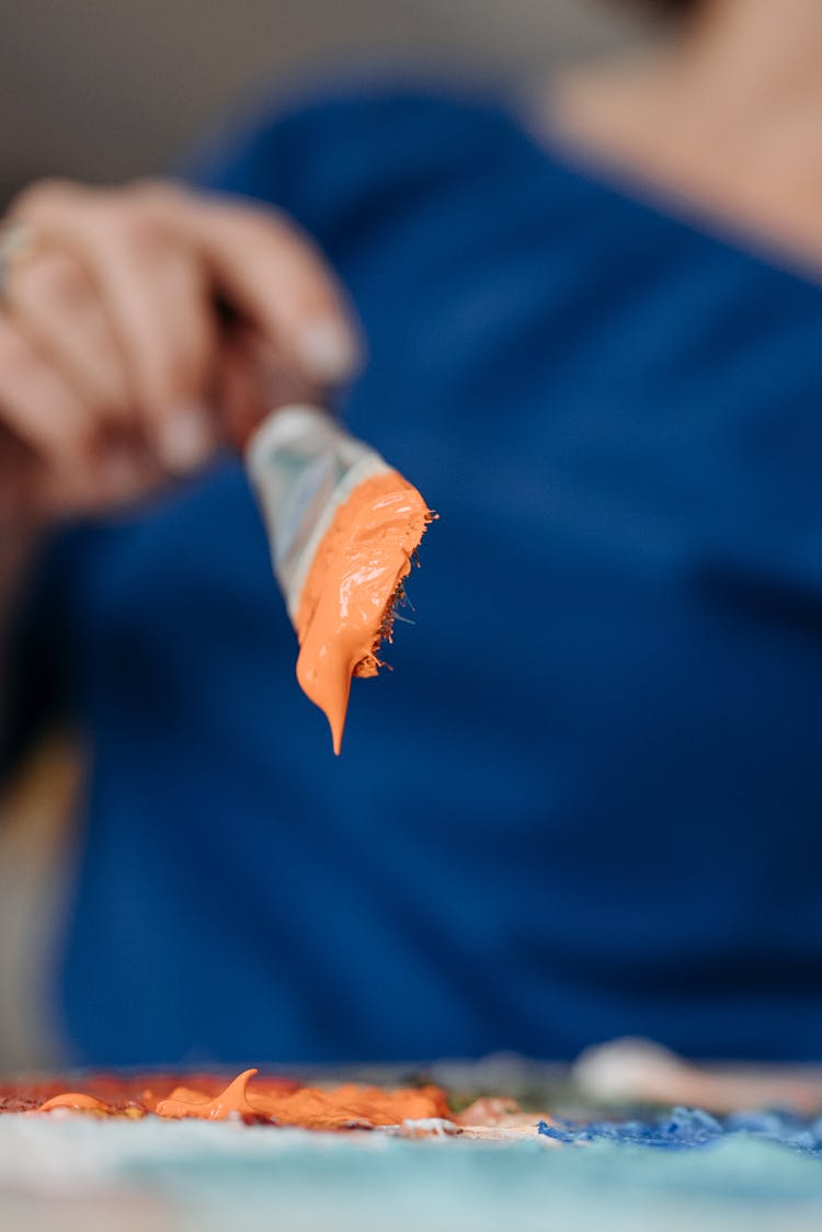 Hand Of Person Holding A Paint Brush With Orange Paint