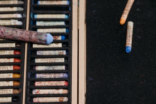 Free Close-up of various colorful oil pastels on a dark textured surface with a pastel box. Stock Photo
