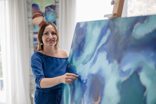 Woman artist presenting an abstract painting in a bright studio environment.