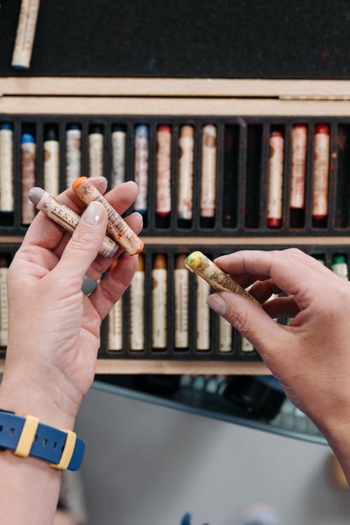 Free Close-up of hands selecting oil pastels from a wooden art case. Ideal for creative or educational themes. Stock Photo